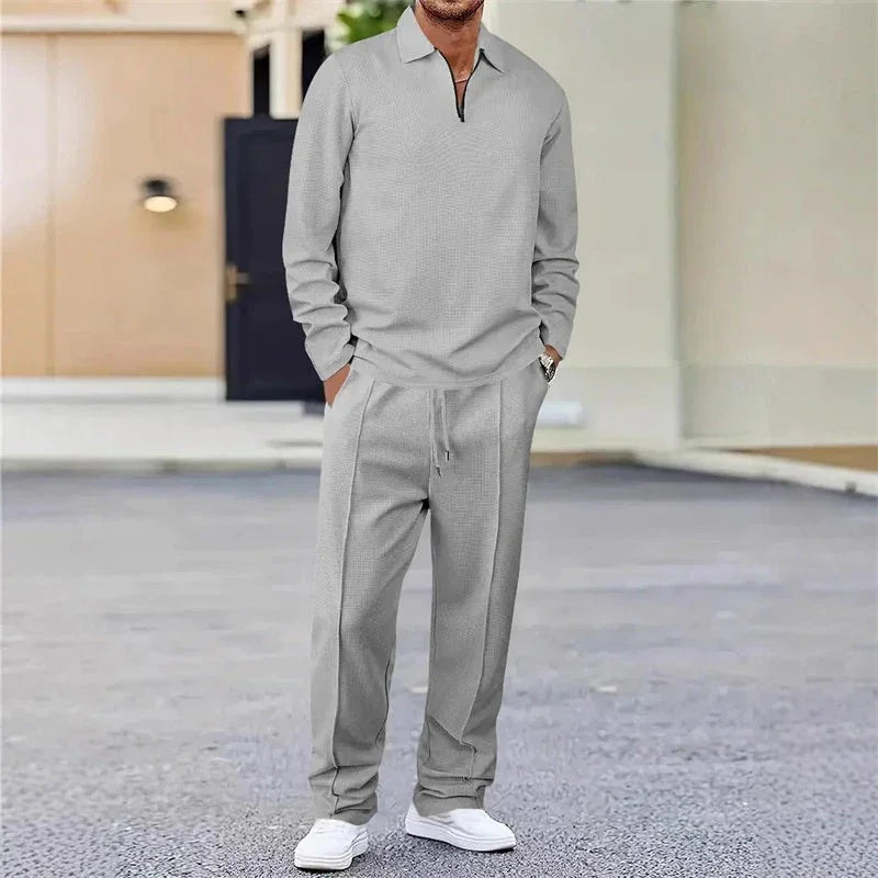 Hombre con conjunto deportivo gris de manga larga y pantalón, zapatillas blancas, exterior urbano