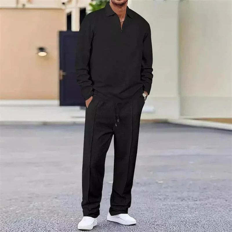 Hombre vistiendo conjunto casual negro de manga larga y pantalón, con tenis blancos, al aire libre