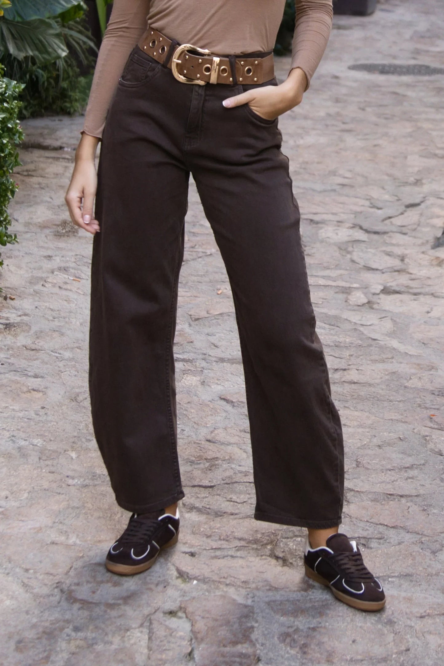 Pantalón marrón de corte recto para mujer, combinado con cinturón ancho y zapatillas negras.