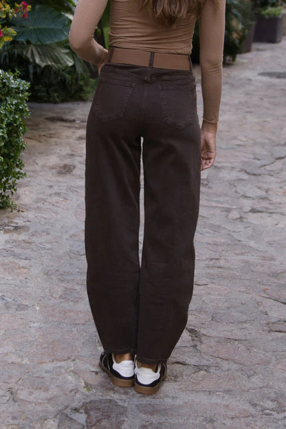 Mujer luciendo pantalón recto café oscuro de mezclilla, vista trasera en exterior empedrado