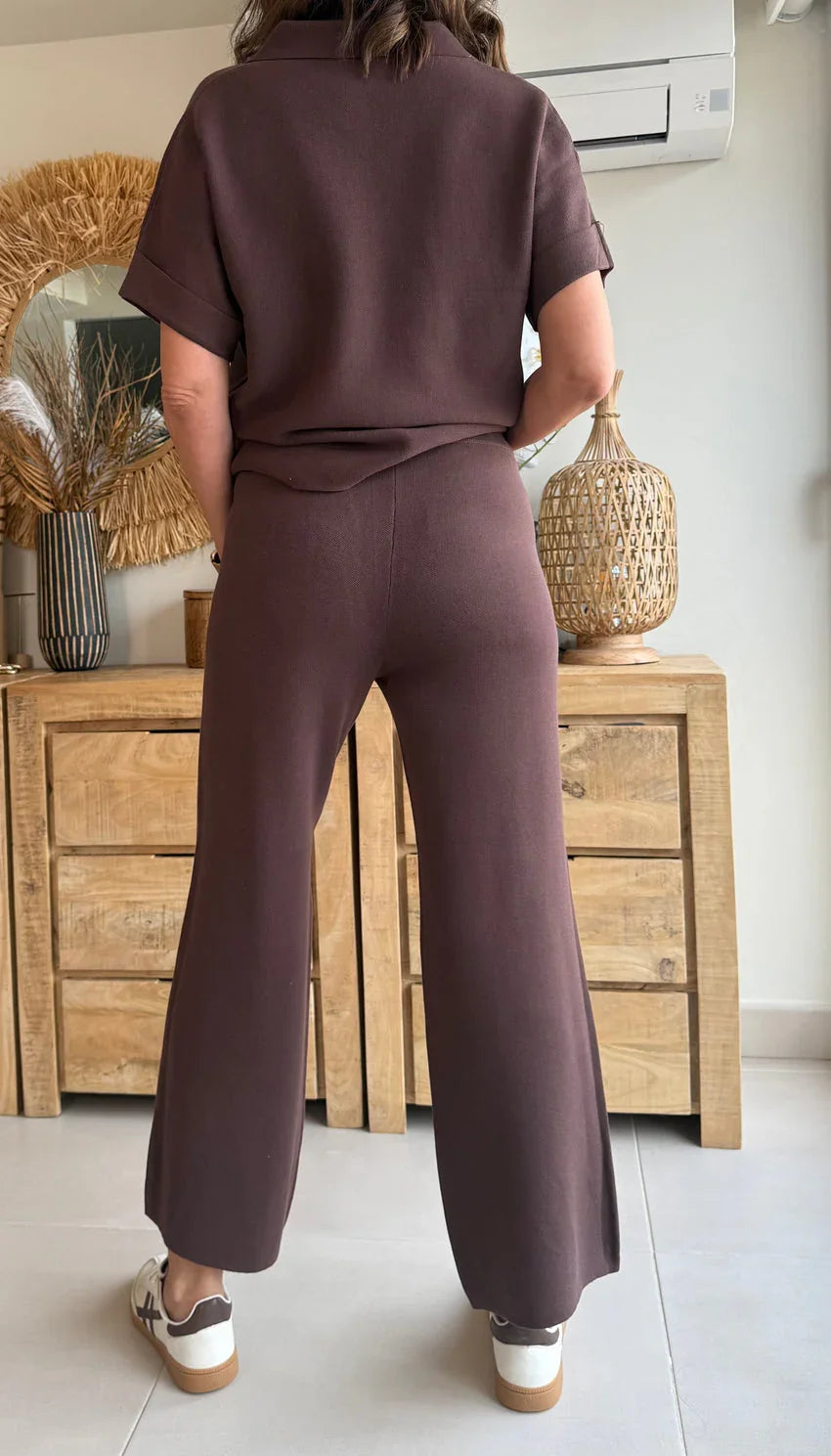 Mujer de espaldas con conjunto marrón de pantalón y camiseta casual, en interior moderno.