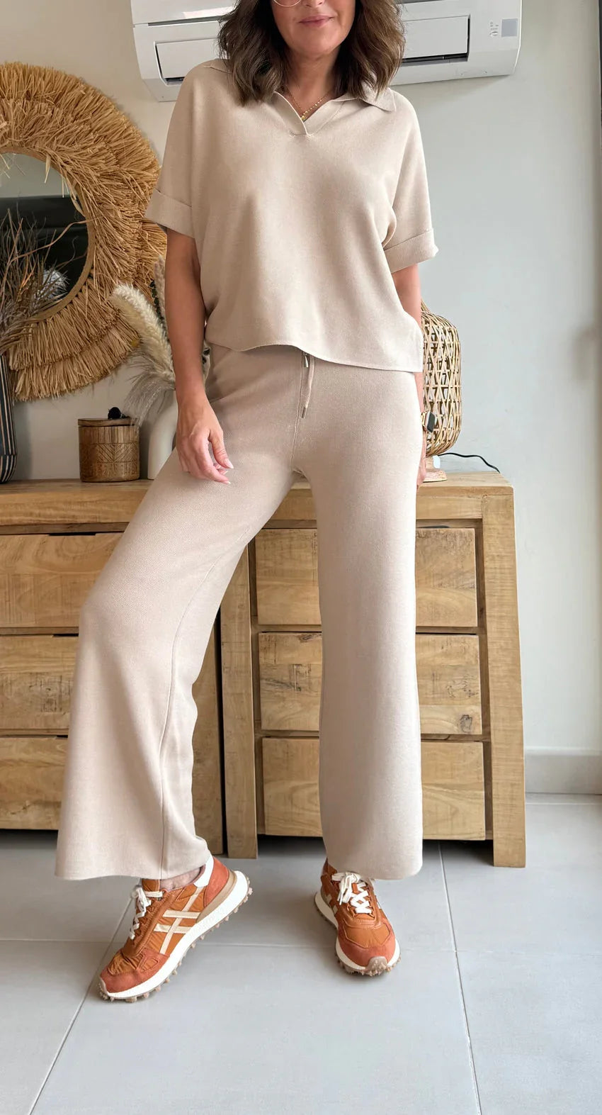 Mujer con conjunto beige relajado y zapatillas deportivas naranjas, en ambiente moderno.