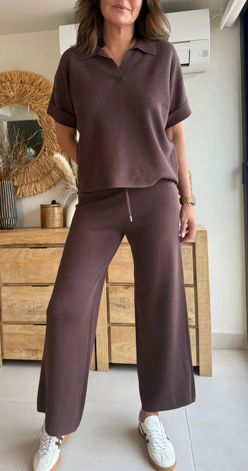 Mujer con conjunto marrón de punto, pantalón holgado y camiseta de manga corta en interior moderno.