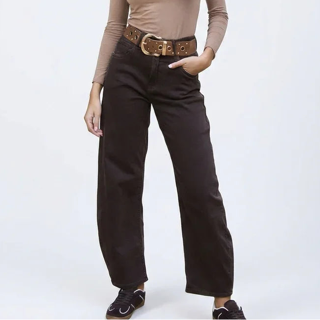 Mujer joven con pantalón marrón ancho, cinturón grande y blusa manga larga beige sobre fondo claro