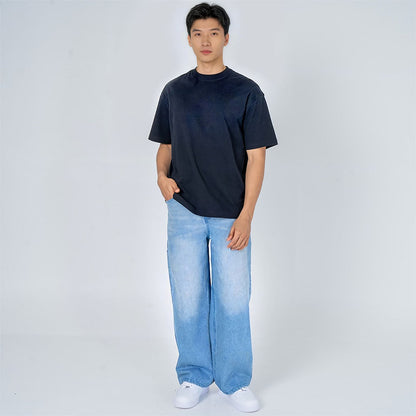 Hombre joven con camiseta negra oversize, jeans anchos celestes y zapatillas blancas, fondo blanco.