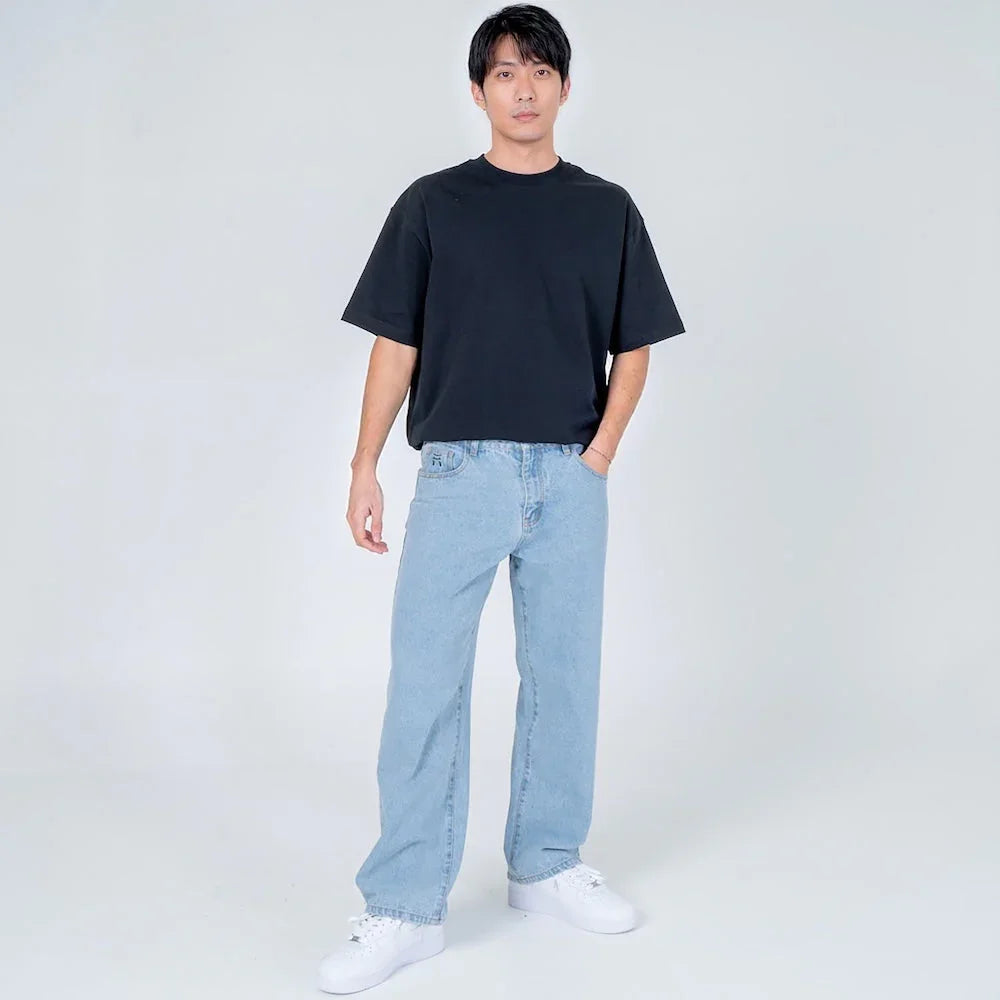 Hombre con camiseta negra oversize y jeans claros rectos en fondo blanco, moda casual masculina