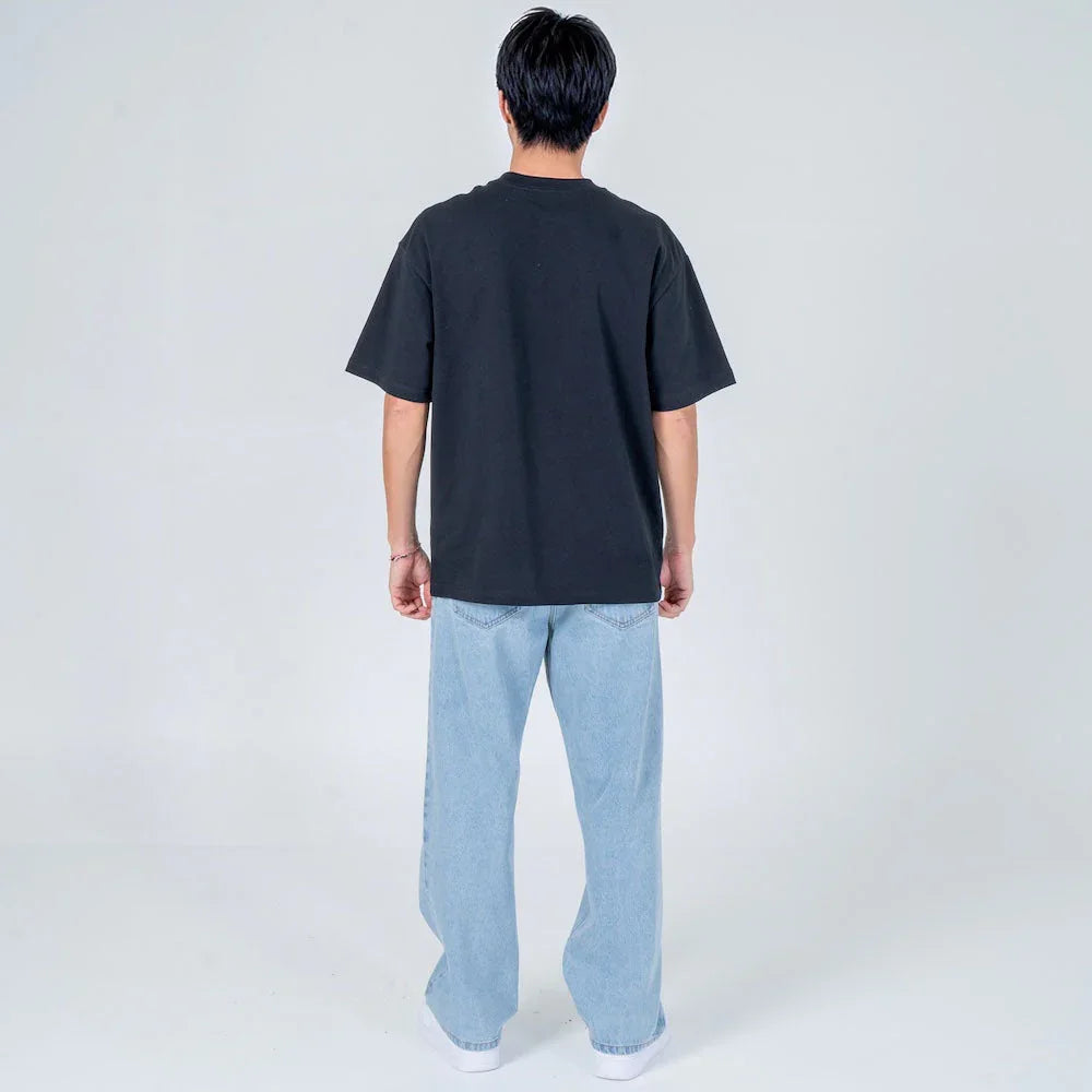 Hombre de espaldas vistiendo camiseta negra y jeans holgados celestes en fondo claro
