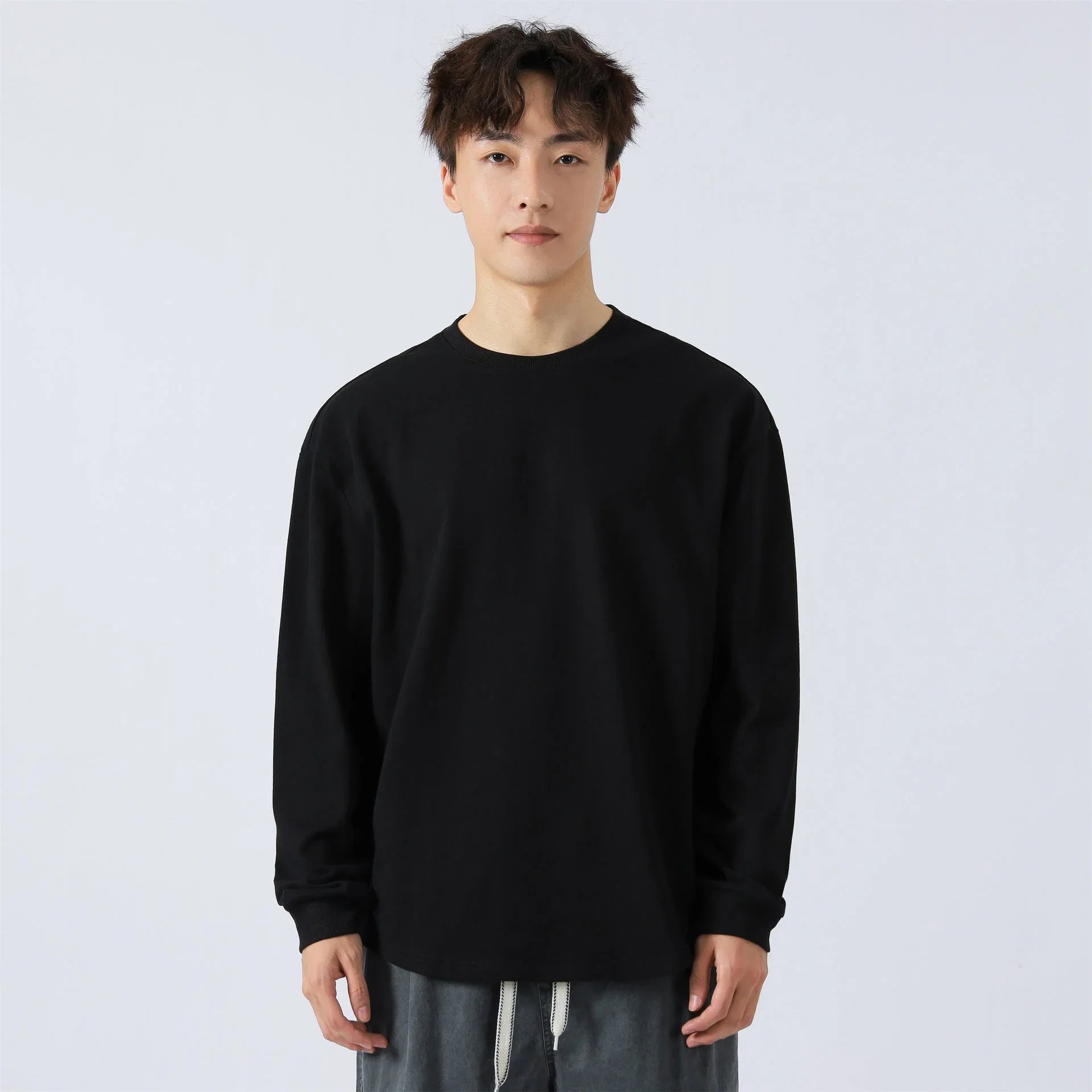 Hombre joven con camiseta negra de manga larga, fondo blanco, ropa casual masculina