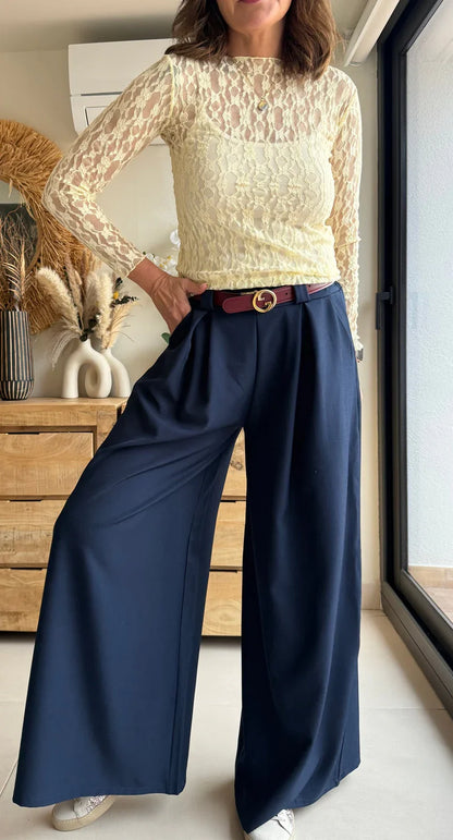 Mujer con blusa de encaje amarillo, pantalón azul marino ancho y cinturón burdeos elegante