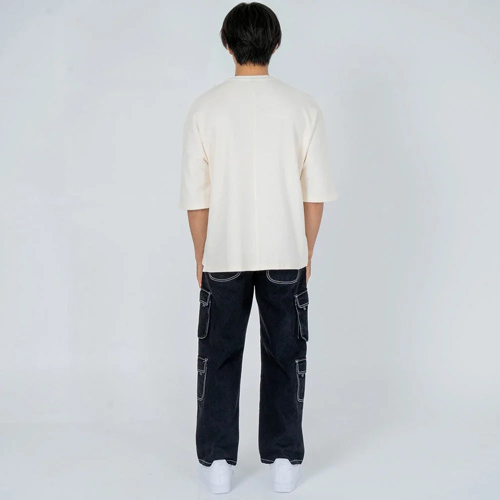 Hombre de espaldas con camiseta beige de manga corta y pantalones cargo negros, fondo blanco