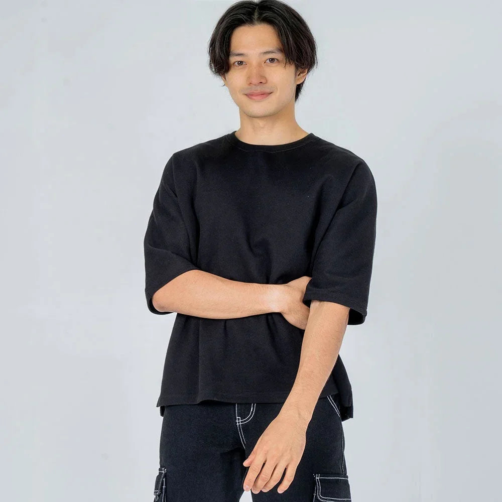 Hombre joven vistiendo camiseta negra de manga media y pantalón oscuro, fondo gris