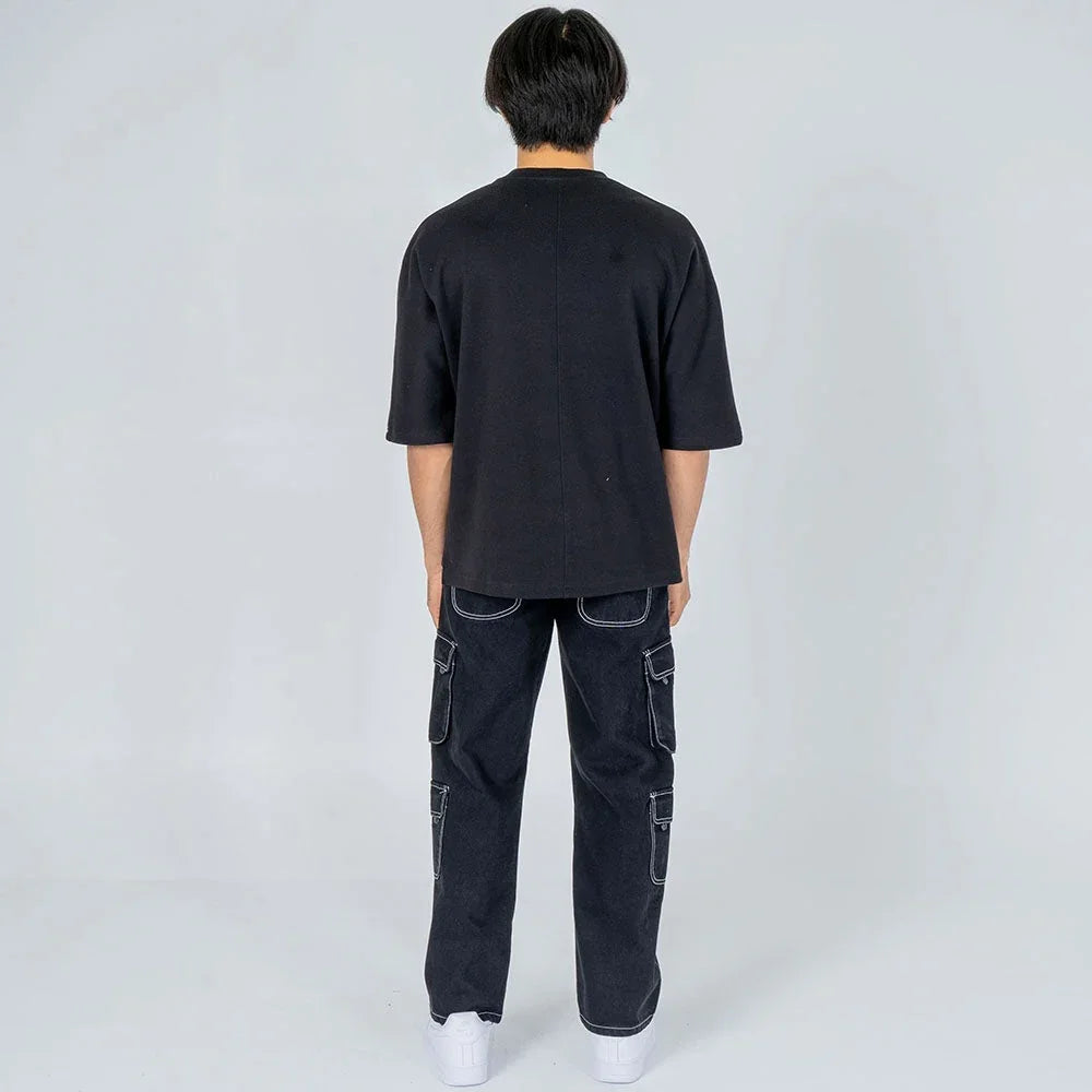 Hombre de espaldas con camiseta negra oversize y pantalón cargo negro, fondo claro