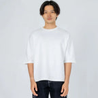 Hombre con camiseta blanca de manga corta y pantalón oscuro sobre fondo claro