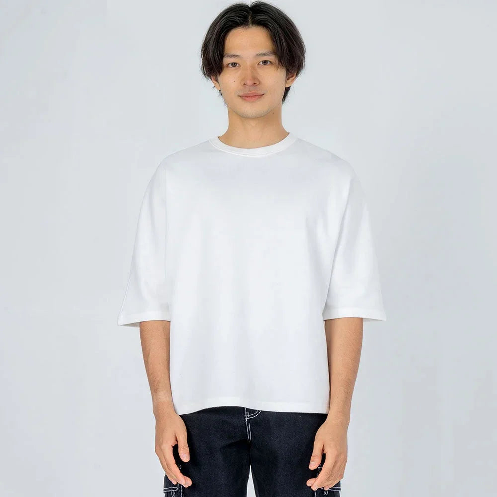 Hombre con camiseta blanca de manga corta y pantalón oscuro sobre fondo claro