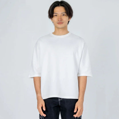 Hombre con camiseta blanca de manga corta y pantalón oscuro sobre fondo claro