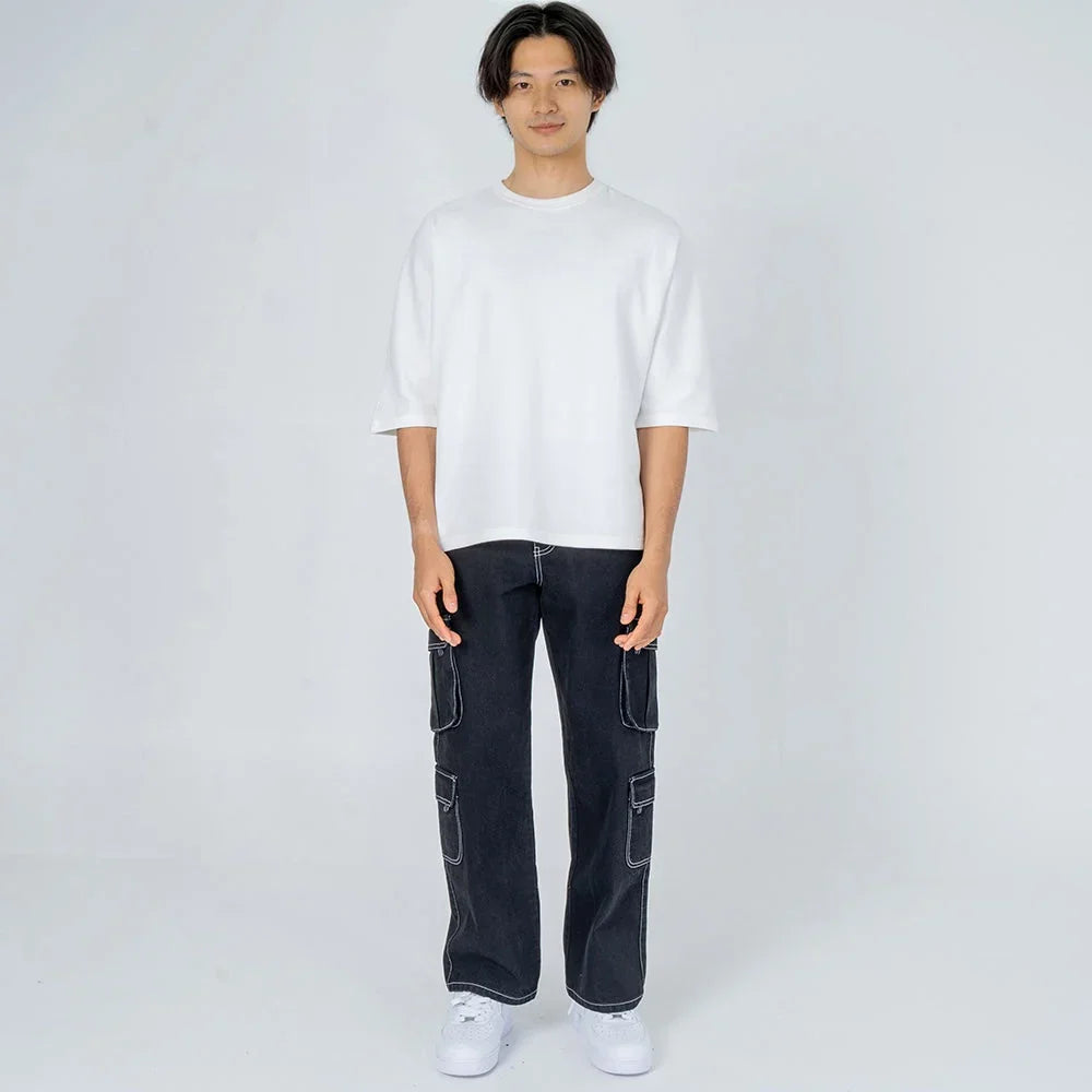 Hombre con camiseta blanca oversize y pantalón cargo negro, fondo blanco minimalista