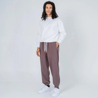 Hombre con sudadera blanca y pantalón jogger gris, calzado deportivo, fondo neutro.
