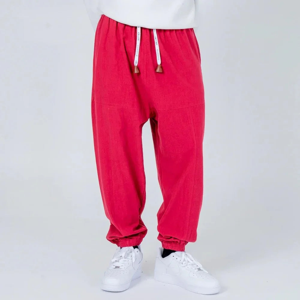 Pantalón jogger rojo con cordón ajustable y puños, calzado blanco, fondo neutro.