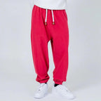 Pantalón jogger rojo con cordón ajustable y puños, calzado blanco, fondo neutro.