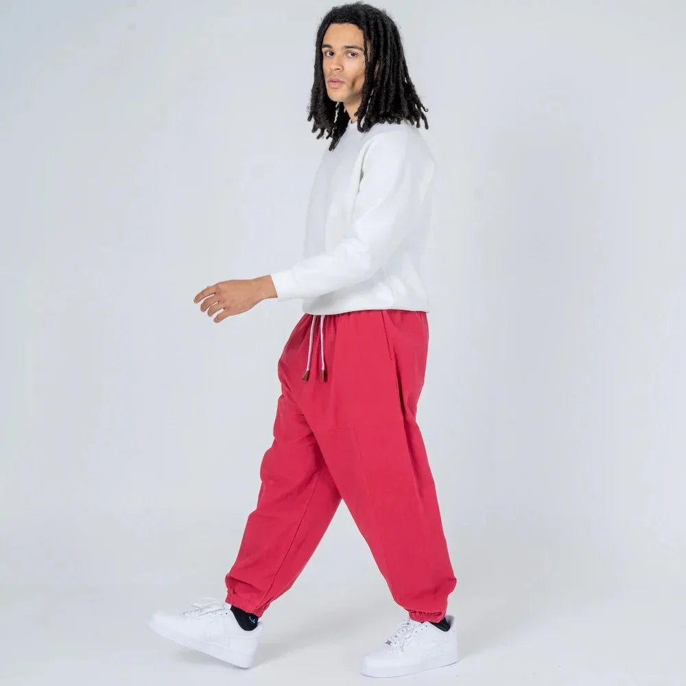 Hombre con pantalones jogger rojos y sudadera blanca en fondo claro