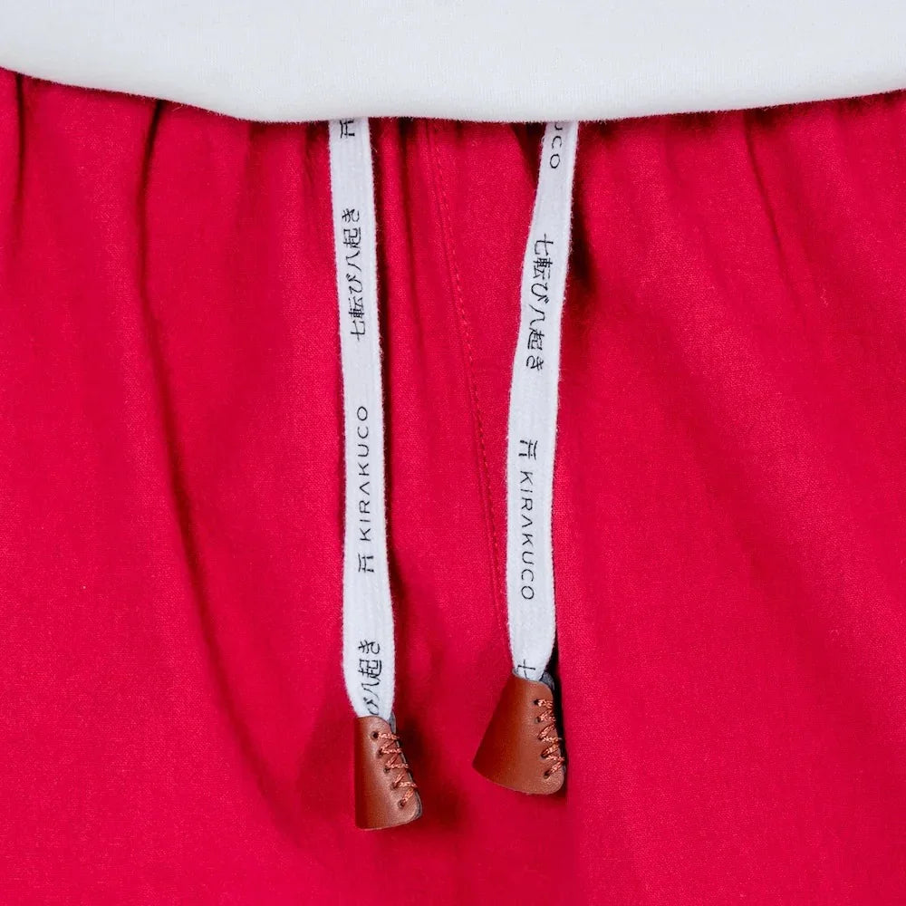 Detalle de pantalón rojo con cordones blancos y letras japonesas, puntas de cuero marrón.
