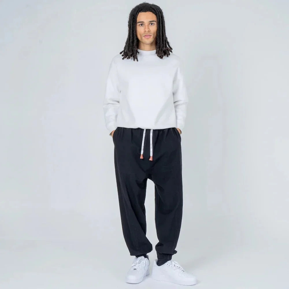 Hombre joven con sudadera blanca y pantalón jogger negro moderno con cordón, fondo blanco