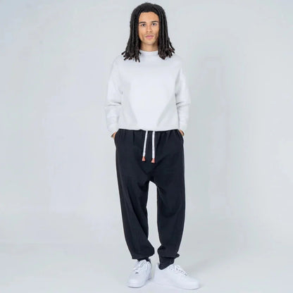 Hombre joven con sudadera blanca y pantalón jogger negro moderno con cordón, fondo blanco