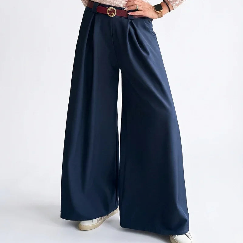 Mujer con blusa de encaje rosa y pantalones palazzo azul marino, fondo blanco.