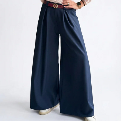 Mujer con blusa de encaje rosa y pantalones palazzo azul marino, fondo blanco.